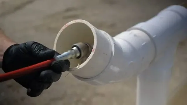 Hand guiding a red jetting hose nozzle into the open end of a PVC pipe
