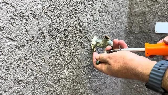 Hand holding a screwdriver and a washer at an outdoor hose bib on a stucco wall