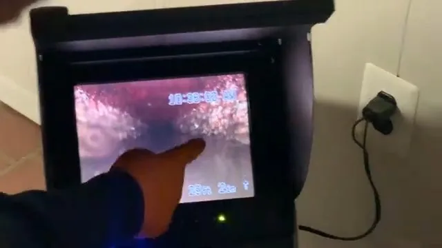 A hand pointing at a pipe interior on a camera monitor that shows a distance counter