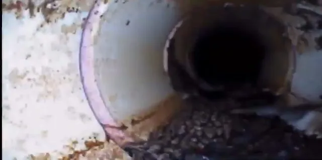 Camera view looking down the inside of a pipe, with a debris pile in the lower part of the frame