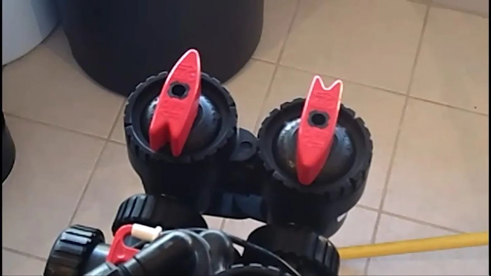 Two black valve heads with red handles on top of a water treatment tank on a tile floor