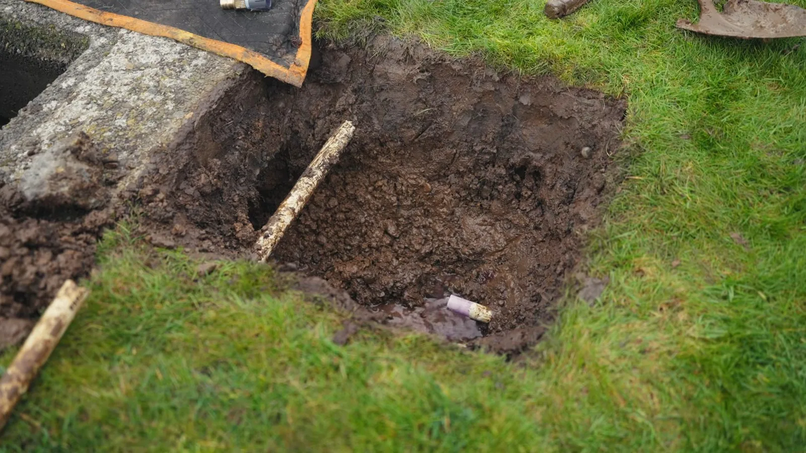 Square hole dug in a lawn with a length of pipe visible at the bottom