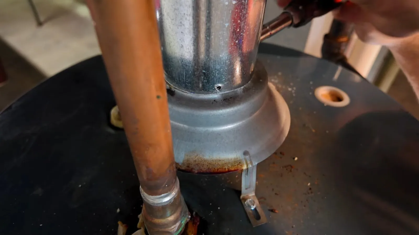 Top of a tank water heater with a flue pipe, copper connections and a torch flame