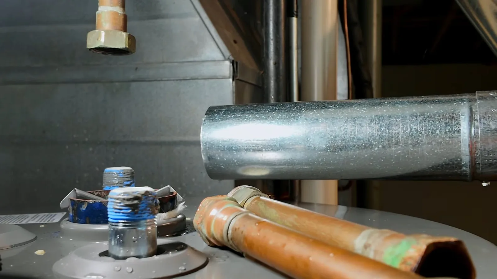 Top of a tank water heater with copper lines, a flue and capped fittings