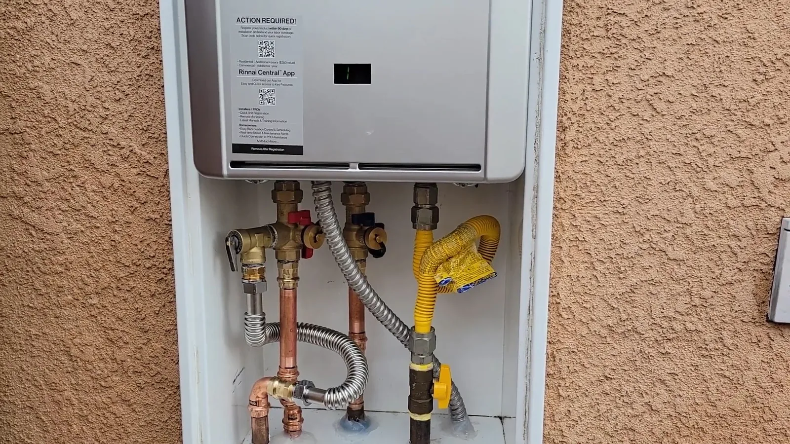 Tankless water heater mounted in a stucco wall box with supply valves and piping below
