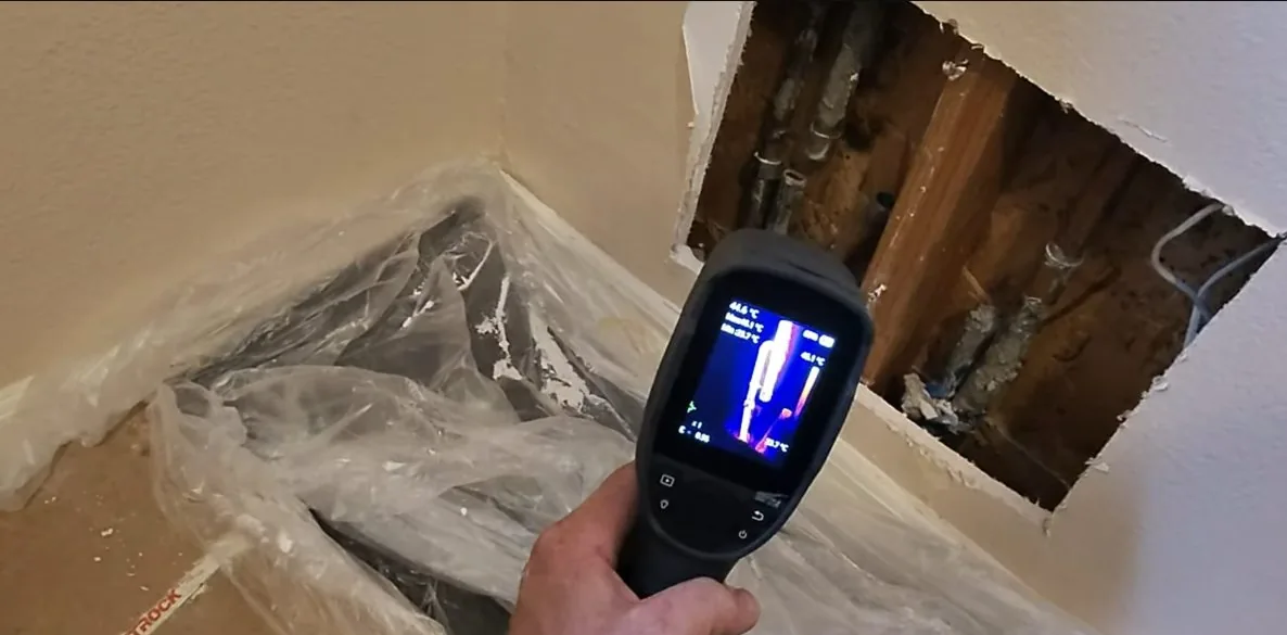 Thermal camera held up to an opened section of wall where pipes are exposed