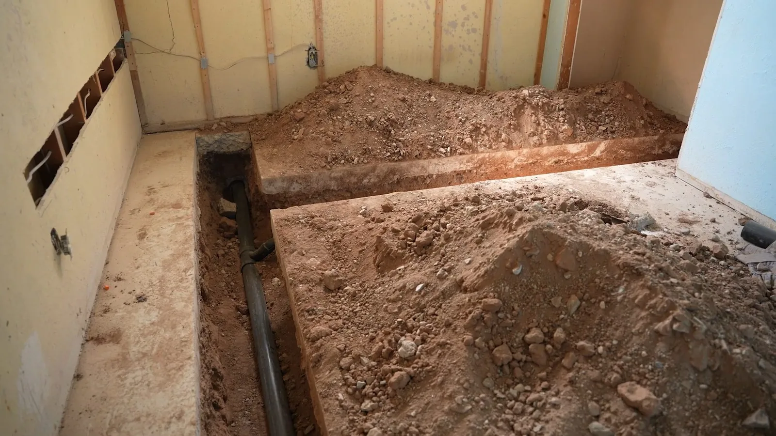 Trench dug across a basement floor with broken concrete along its edges