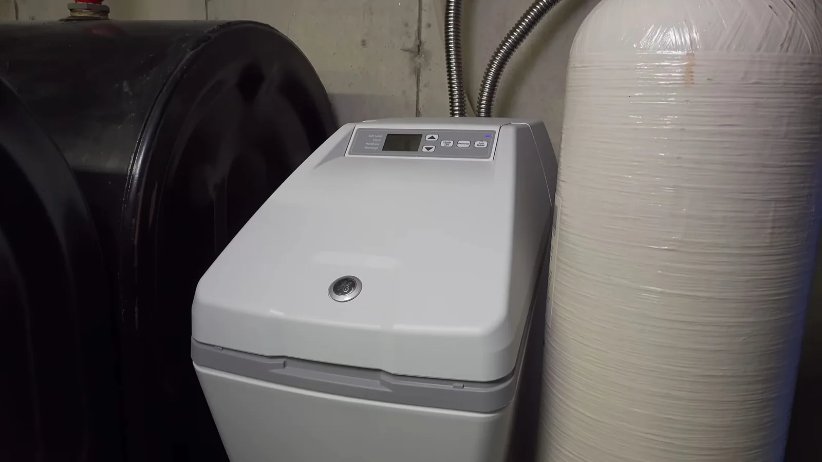 Grey water softener beside a black brine tank and a white tank in a utility room