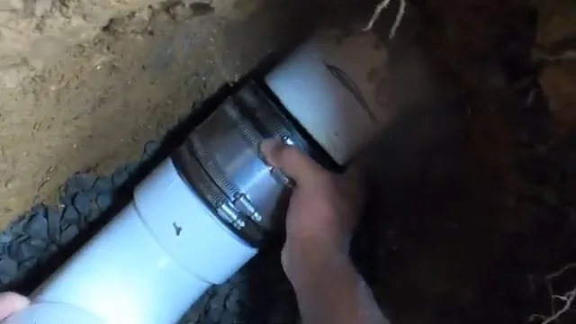 Hand tightening a rubber coupling clamp on a white PVC pipe lying in a trench