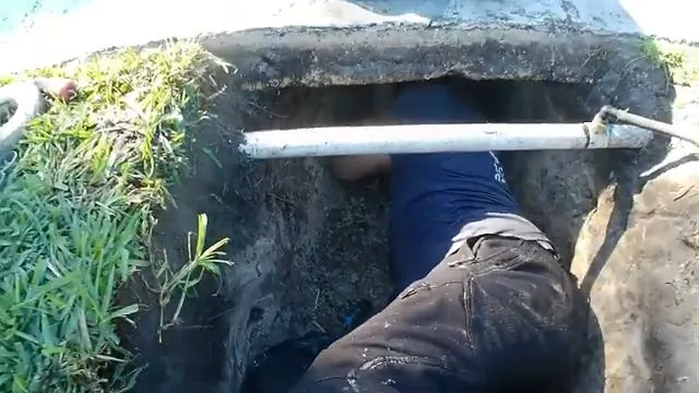 Worker in a shallow excavation in a lawn beside a length of white pipe