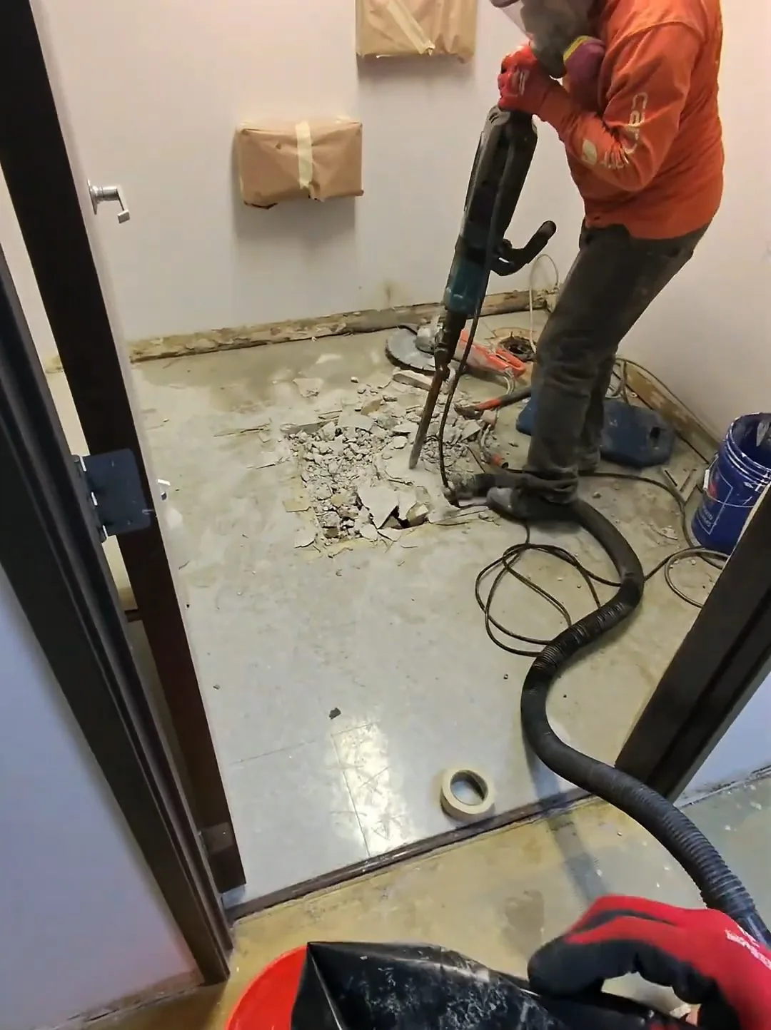 Worker in an orange hoodie breaking up a bathroom floor with a jackhammer