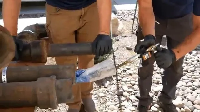 Two workers beside sections of cast iron pipe and a liner sleeve laid out on gravel